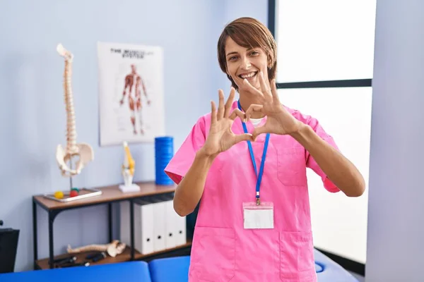 Brunette Woman Working Rehabilitation Clinic Smiling Love Doing Heart Symbol — Stok Foto