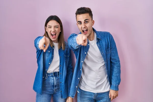 Young Hispanic Couple Standing Pink Background Pointing Displeased Frustrated Camera — Stockfoto