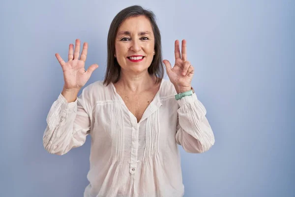 中年ヒスパニック女性立っています上の青の背景ショーと指番号8を指している間に笑顔自信と幸せ — ストック写真