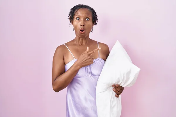African Woman Dreadlocks Wearing Pajama Hugging Pillow Surprised Pointing Finger — 图库照片