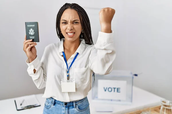 Young african american woman at political campaign election holding usa passport annoyed and frustrated shouting with anger, yelling crazy with anger and hand raised