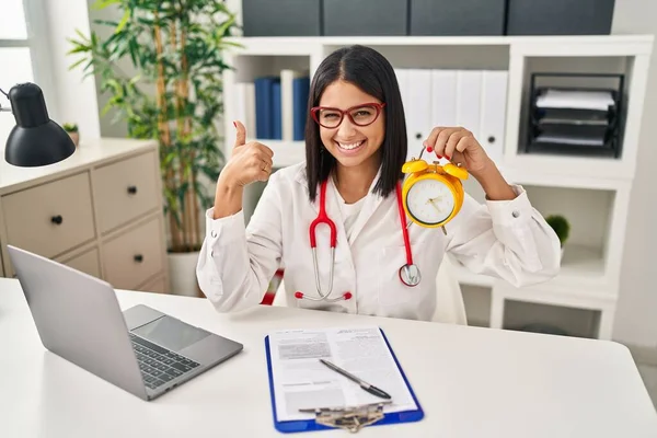 Joven Doctora Hispana Sosteniendo Despertador Clínica Sonriendo Feliz Positiva Pulgar — Foto de Stock