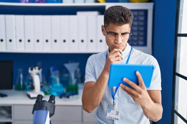 Young Hispanic Man Scientist Using Touchpad Doubt Expression Laboratory — Stock Photo, Image