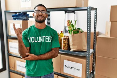 Genç Hintli gönüllü bağış kutusu tutuyor. Yüzünde kocaman bir gülümseme var. Eli ve parmağı kameraya bakıyor.. 