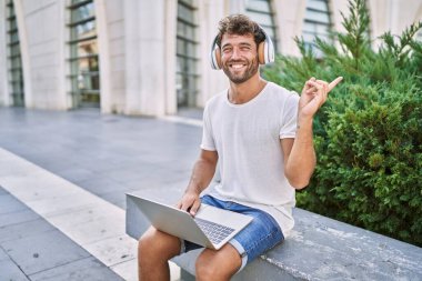 Sokakta kulaklık ve dizüstü bilgisayar kullanan genç İspanyol adam gülümsüyor. 
