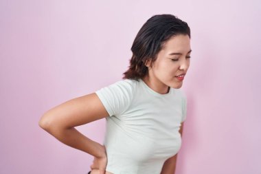 Hispanic young woman standing over pink background suffering of backache, touching back with hand, muscular pain 
