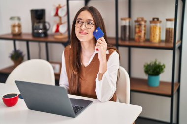 Evdeki masada dizüstü bilgisayar ve kredi kartı kullanan genç ve güzel bir İspanyol kadın.