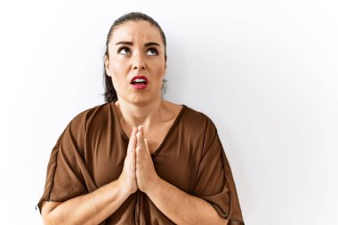 Genç esmer kadın izole edilmiş arka planda duruyor. Elleriyle yalvarıyor ve dua ediyor. Yüzünde umut ifadesi var. Yalvarıyor. 