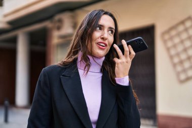 Young hispanic woman smiling confident listening audio message by the smartphone at street