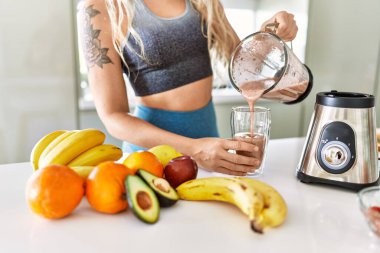Genç bir kadın mutfakta cama smoothie döküyor.