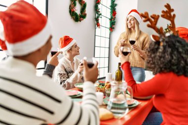 Mutlu bir şekilde gülümseyen bir grup genç Noel yemeği yiyor ve evde kadeh kaldırıyor..