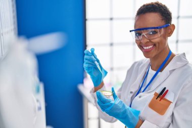 Afrikalı Amerikalı bilim kadını gülümsüyor. Laboratuvarda kendine güveni tam bir sıvı döküyor.