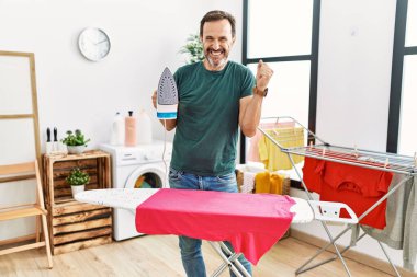 Sakallı orta yaşlı bir adam evde kıyafetlerini ütülüyor gururla bağırıyor, zaferi kutluyor ve kollarını kaldırdığı için çok heyecanlı. 