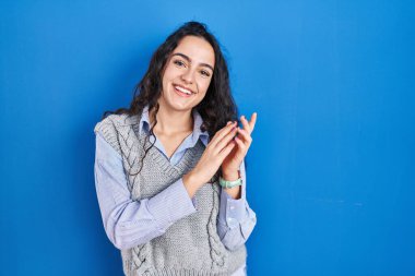 Genç esmer kadın mavi arka planda ayakta alkışlıyor ve mutlu ve neşeli alkışlıyor, gururla gülümsüyor. 