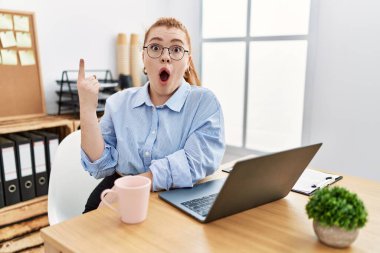 Ofiste çalışan genç kızıl saçlı kadın bilgisayarla başarılı bir fikri işaret ediyor. Heyecanlı ve mutlu. Bir numara.. 