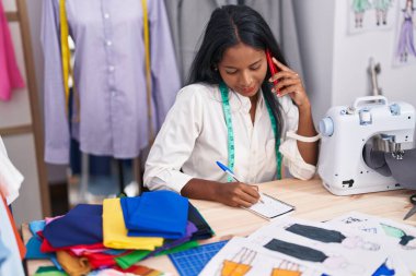 Terzide akıllı telefondan konuşan genç ve güzel bir kadın terzi.