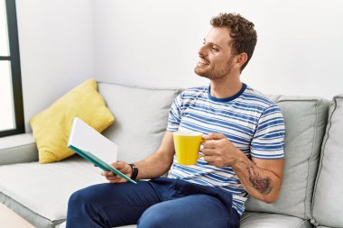 Genç İspanyol adam kahve içiyor ve evde kitap okuyor.