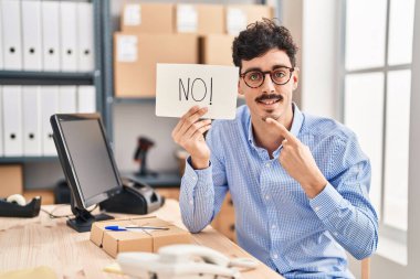 Hispanic man working at small business ecommerce holding no banner smiling happy pointing with hand and finger 