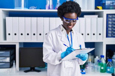 Young african american woman scientist writing on document at laboratory