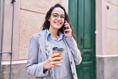 Genç İspanyol kadın yönetici kahve içiyor ve caddede akıllı telefondan konuşuyor.
