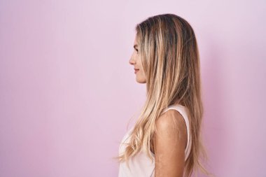 Pembe arka planda duran genç sarışın kadın yan bakıyor, rahat poz veriyor doğal bir yüz ve kendine güvenen bir gülümsemeyle.. 