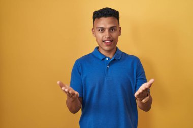 Sarı arka planda duran genç İspanyol adam gülümseyen, yardım eli uzatan ve kabul gören biri.. 