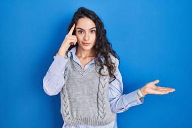 Mavi arka planda dikilen esmer kadın avuç içinin açık olmasından rahatsız ve kafası karışmış bir şekilde fotokopi alanını gösteriyor ve alnını işaret ediyor. Bunu bir düşün.. 