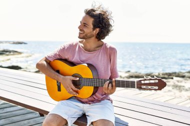 Genç İspanyol adam klasik gitar çalıyor sahilde bankta oturuyor..