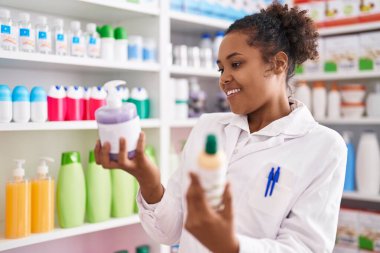African american woman pharmacist smiling confident holding gel bottles at pharmacy