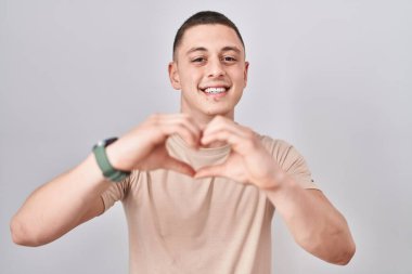 İzole edilmiş arka planda duran genç adam, aşka gülümseyip elleriyle kalp sembolü çiziyor. romantik kavram. 