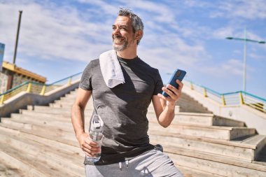 Orta yaşlı İspanyol adam spor giyer. Sokakta akıllı telefon kullanır.