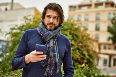 Parkta akıllı telefon kullanan orta yaşlı yakışıklı bir adam.