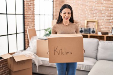 Young woman moving to a new home holding box smiling and laughing hard out loud because funny crazy joke. 