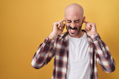 Sarı arka planda duran İspanyol sakallı adam yüksek sesli müzik sesi için kulaklarını parmaklarıyla kapatıyor. sağır kavramı. 