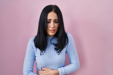 İspanyol kadın, midesi üstünde pembe arka planda duruyor çünkü hazımsızlık, acı verici bir hastalık kendini iyi hissetmiyor. Ağrı kavramı. 