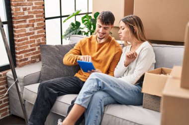 Young man and woman couple using touchpad sitting on sofa at new home