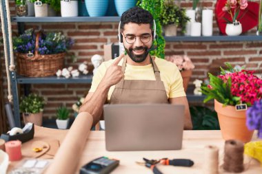 Hispanic man with beard working at florist shop doing video call smiling happy pointing with hand and finger 
