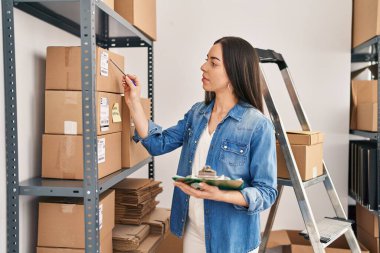 Young beautiful hispanic woman ecommerce business worker writing on document at office