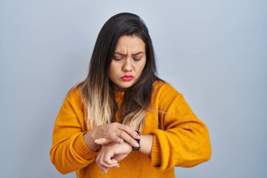 Tecrit edilmiş arka planda duran genç İspanyol kadın saati kontrol ediyor, rahat ve kendinden emin. 