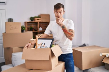 Caucasian man holding screwdriver at new home serious face thinking about question with hand on chin, thoughtful about confusing idea 