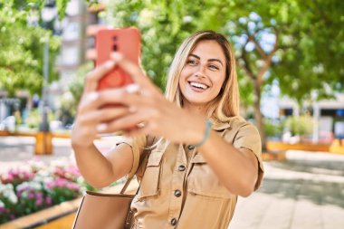 Young blonde girl smiling happy making selfie by the smartphone at the city.