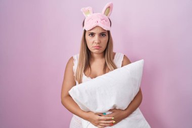 Young blonde woman wearing pyjama hugging pillow depressed and worry for distress, crying angry and afraid. sad expression. 