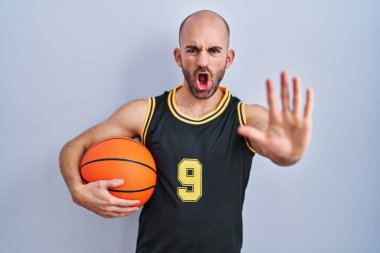 Sakallı, basketbol forması giyen, elinde top tutan, avuç içi hareketi yapan, sinirli ve hayal kırıklığına uğramış genç, kel bir adam. 