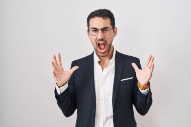 Handsome business hispanic man standing over white background celebrating mad and crazy for success with arms raised and closed eyes screaming excited. winner concept 