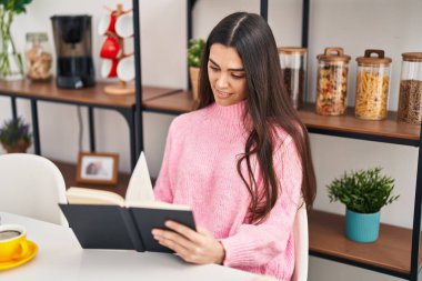 Genç İspanyol kadın kitap okuyor, kahvaltısını evde yapıyor.