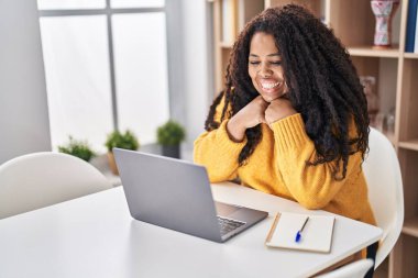 Evde masada dizüstü bilgisayar kullanan Afrikalı Amerikalı bir kadın.