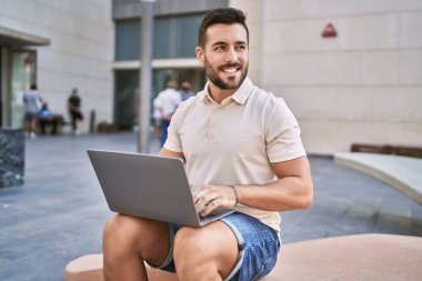 Sokakta dizüstü bilgisayar kullanarak gülümseyen İspanyol genç adam.