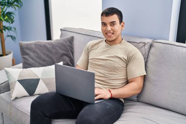 Evde kanepede otururken dizüstü kullanan genç adam