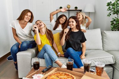 Group of young woman friends having party eating italian pizza and singing song at home.