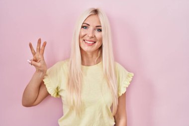 Caucasian woman standing over pink background showing and pointing up with fingers number three while smiling confident and happy. 